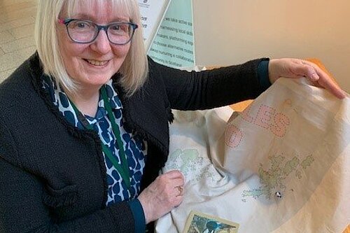 Beatrice Wishart shows a cloth with a map of Scotland on it with a button she sewed onto Shetland