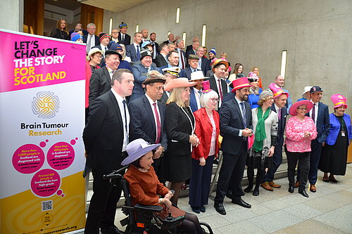MSPs stand in rows in the Scottish Parliament wearing hats